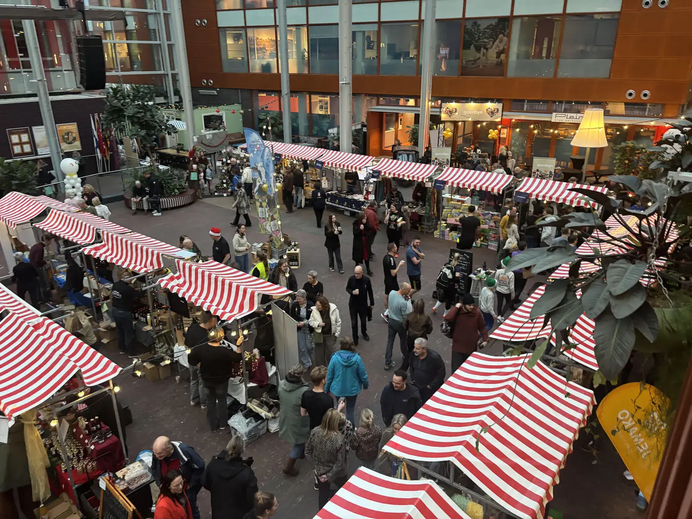 Overzicht van een DROP-personeelskerstmarkt: marktkramen met rood-witte luifels en medewerkers in het atrium van de organisatie